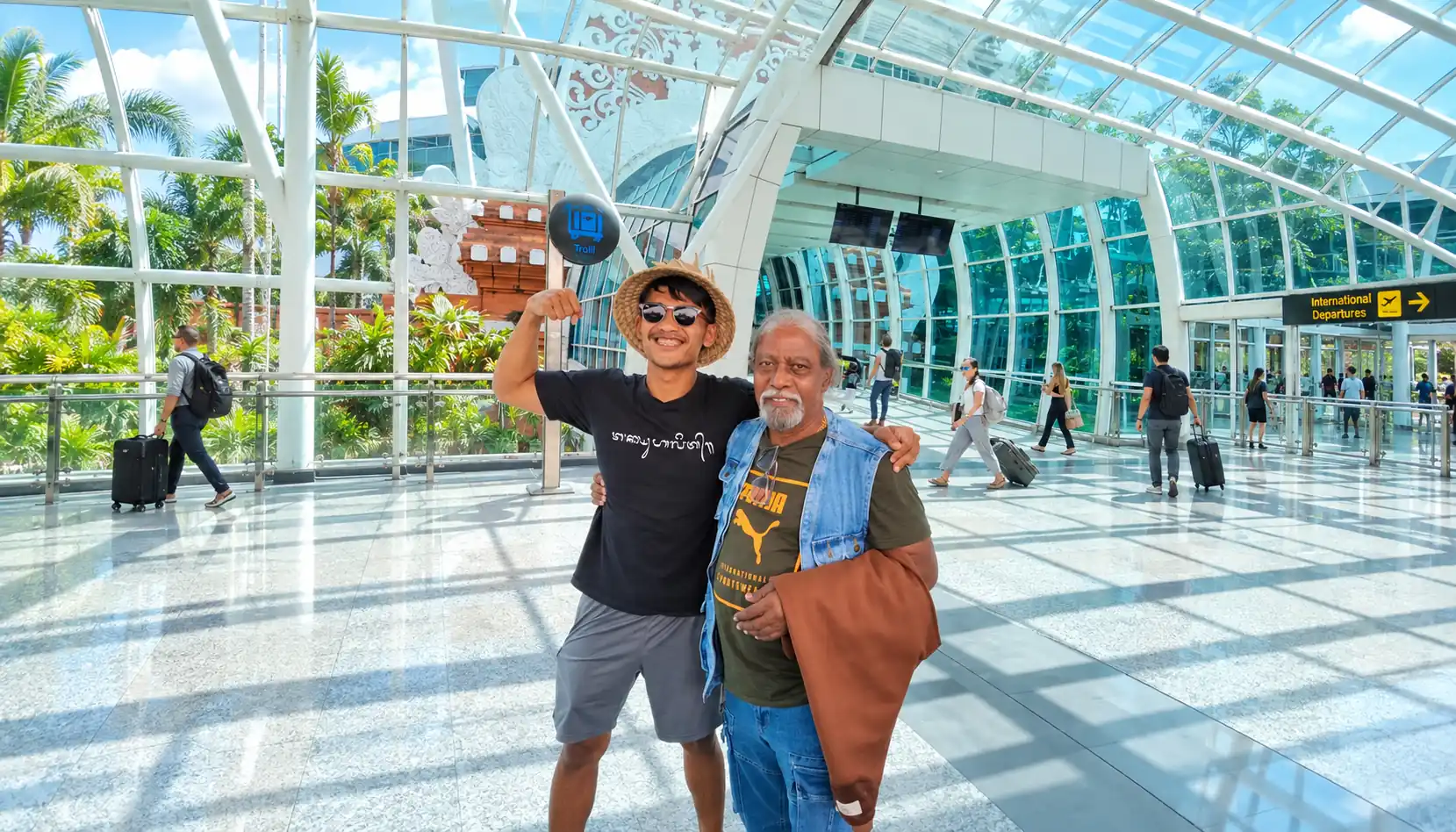 Two men posing together in the sunlit terminal at Ngurah Rai Airport