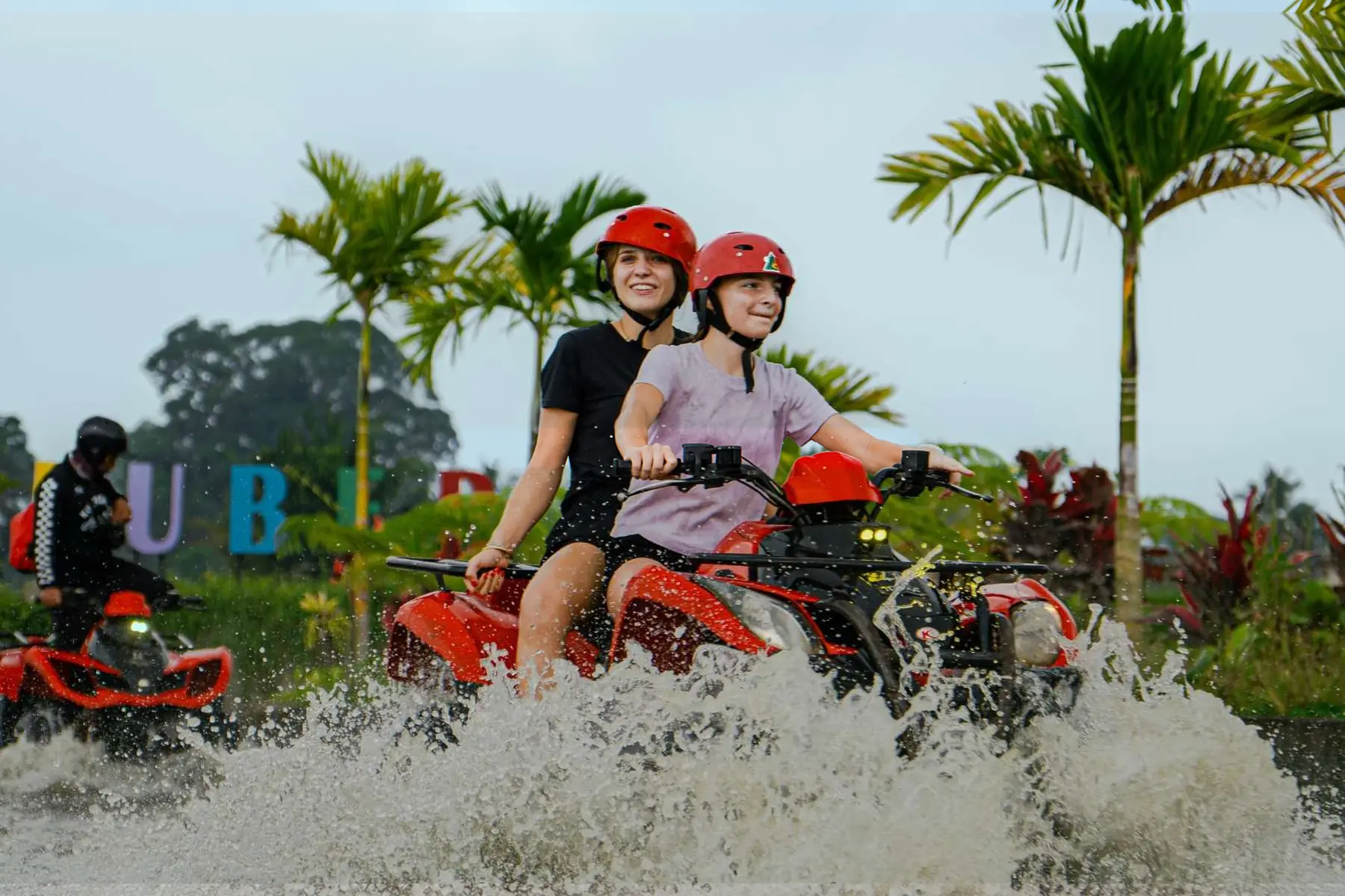 Two helmeted riders on a Kuber ATV splashing through water