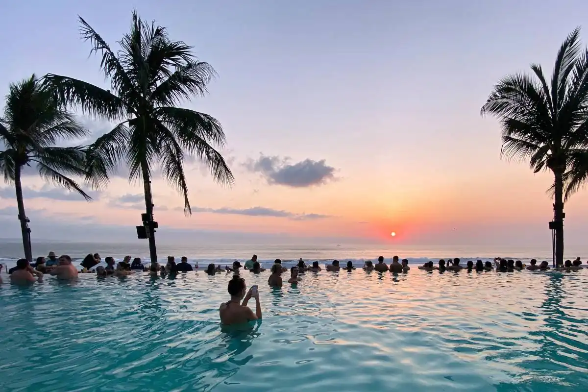 Guests enjoying a palm-lined seaside pool at sunset